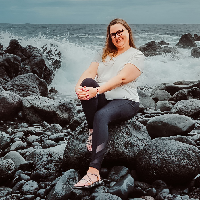 Smiling person sitting on rock by ocean waves.