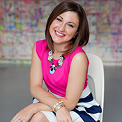 Woman smiling in colorful outfit, sitting indoors.