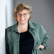 Smiling person wearing glasses and green jacket.